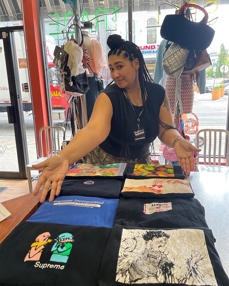 graphic-tees Manager poses with arms open gesturing to graphic tees displayed on table