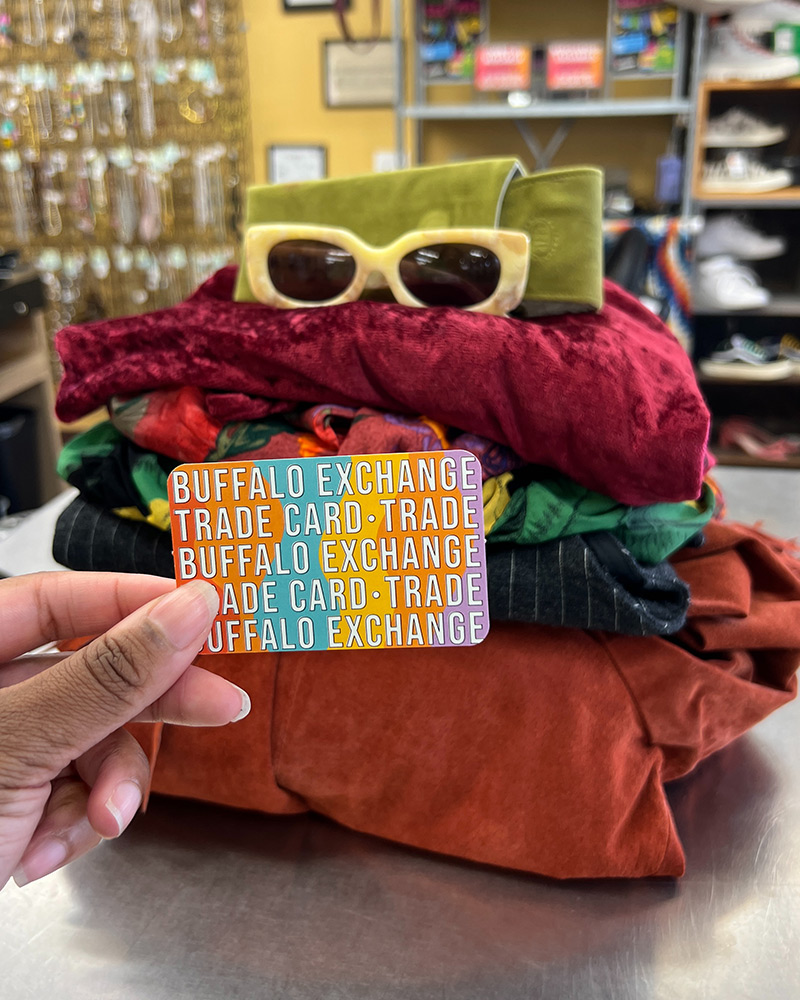 trade-card Stack of clothing with hand holding Buffalo Exchange trade card