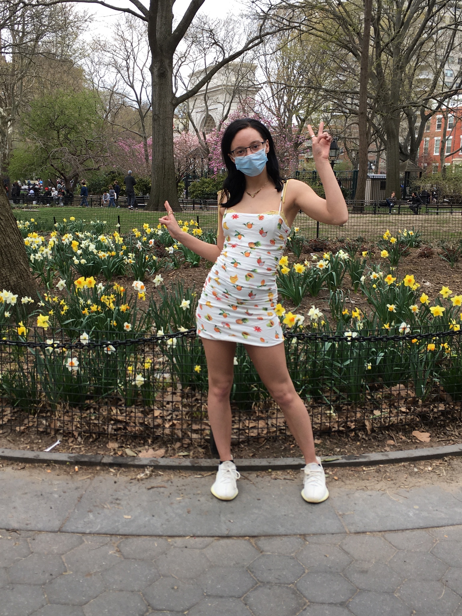 person standing in front of flower bushes wears fruit printed white slip dress and casual white sneakers