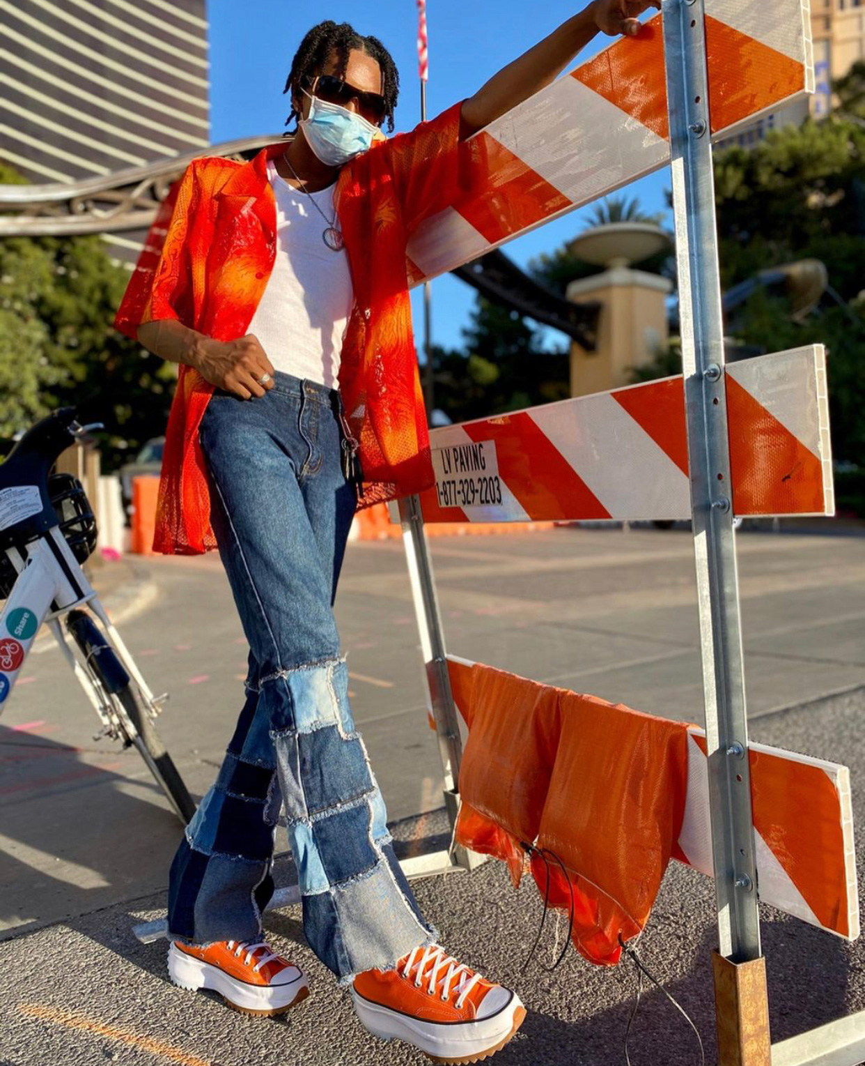 Katriel wearing an unbuttoned orange short-sleeve button down, white t-shirt, patchwork denim flares, and orange Converse sneakers