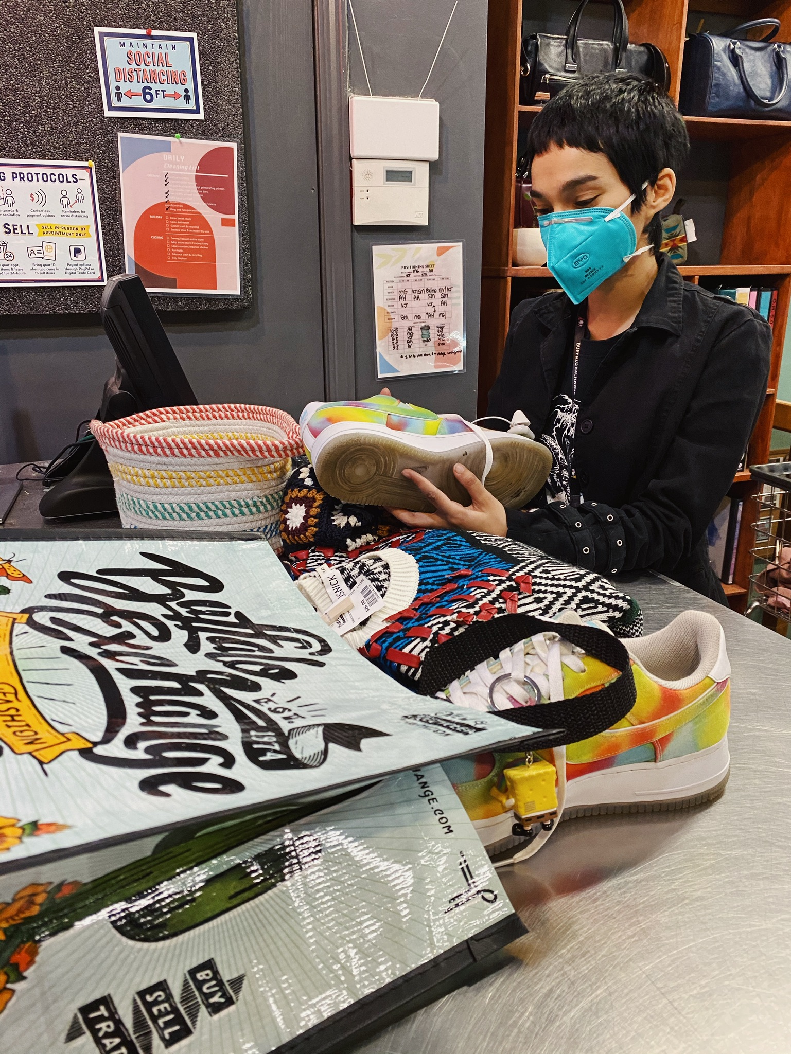 Buffalo Exchange employee behind Buy Counter reviews a pair of tie-dye Nike sneakers from a customer's buy