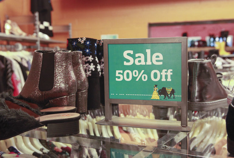 Man standing inside in front of shoe racks with foot up on bench wearing a yellow polo tee and green checkered socks