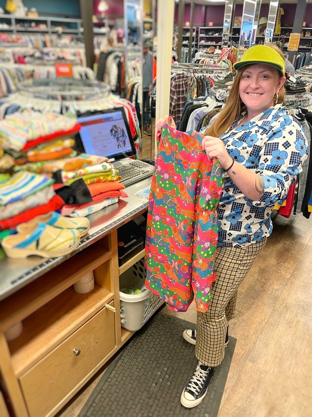 Buffalo Exchange Buyer holds up a piece of clothing behind a large stack of clothes on the counter