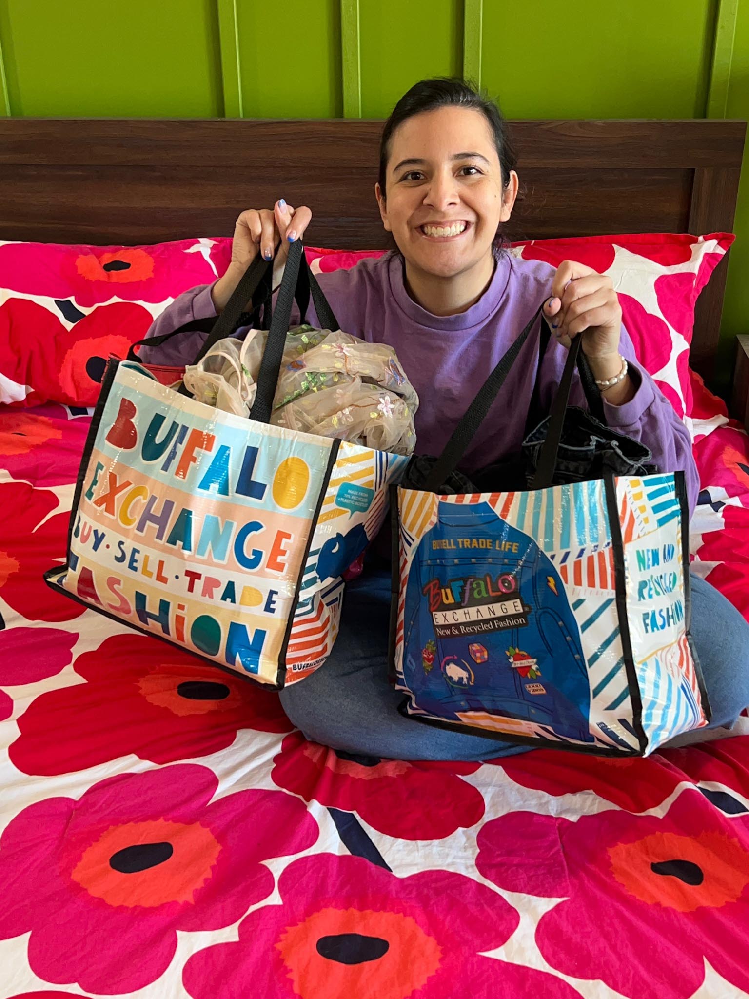 Happy seller sitting on bed with bags of clothes in Buffalo Exchange totes