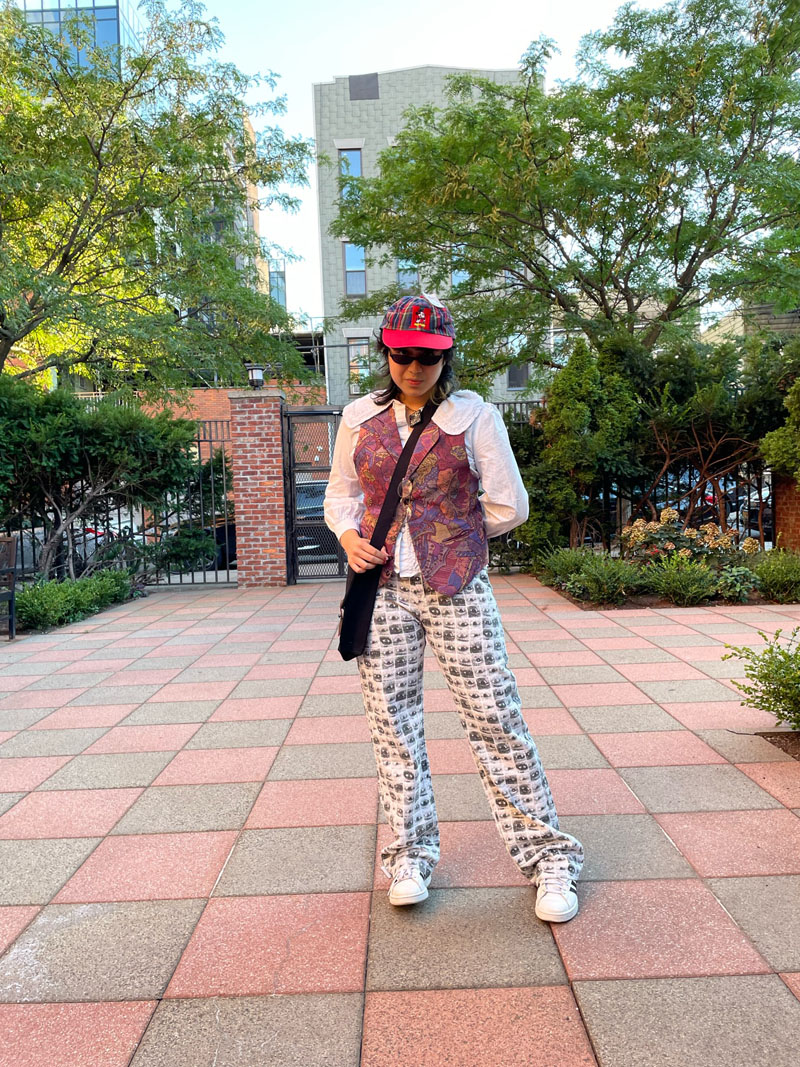 Person standing in courtyard wearing paisley vest and eye-printed jeans