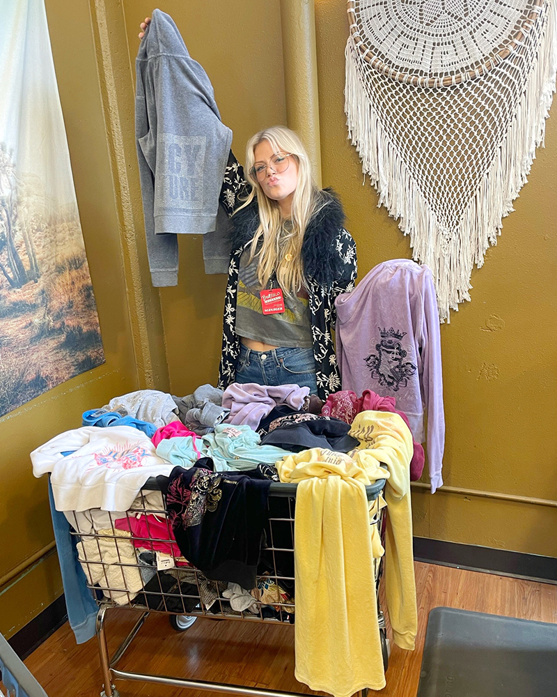 A person holding hoodies stands over a rolling basket full of clothing