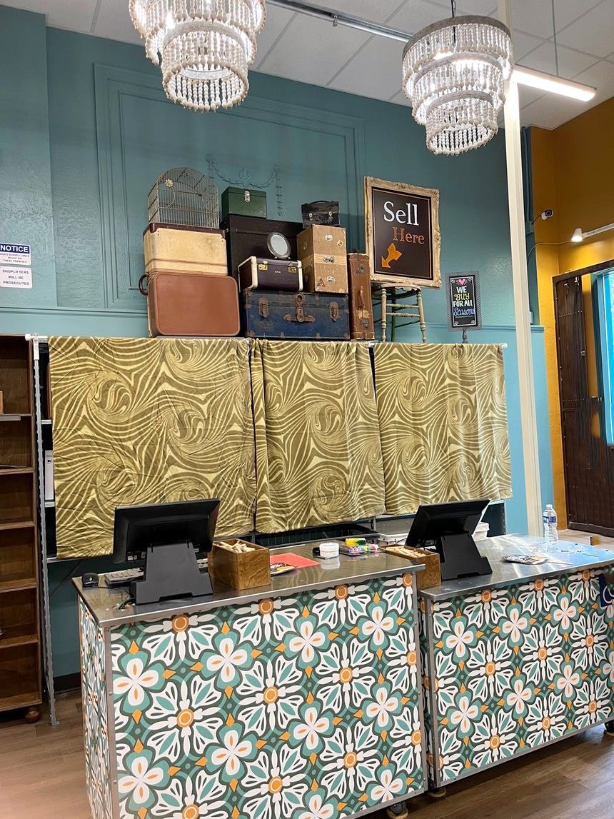 Tiled store counter with computers in front of sign that reads "Sell Here" with an arrow