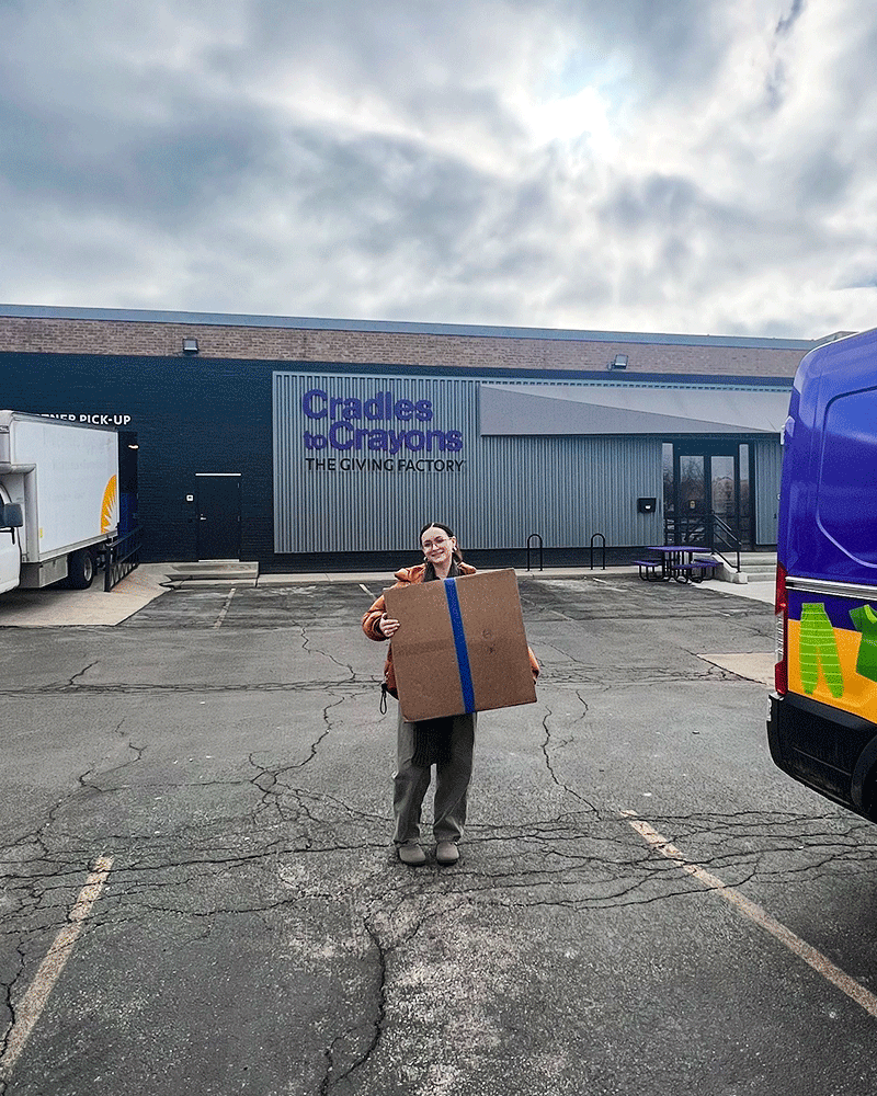 Employee holding donation box in front on Cradles to Crayons building