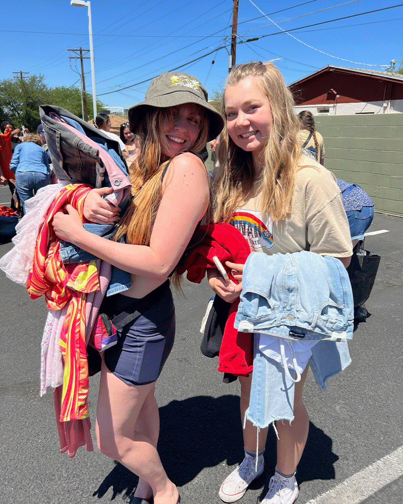 Two customers holding piles of clothes in hand pose for photo outside