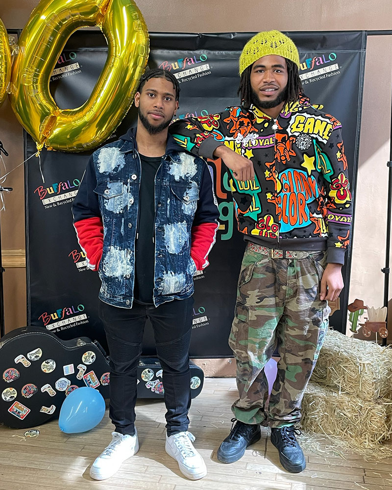 2 people posing in front of logoed Buffalo Exchange backdrop