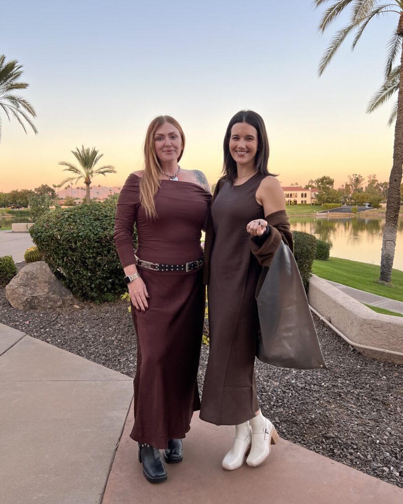 2024.11 Company Meeting Fashion (81).JPG Two women wearing brown semi formal outfits pose in front of the sunset