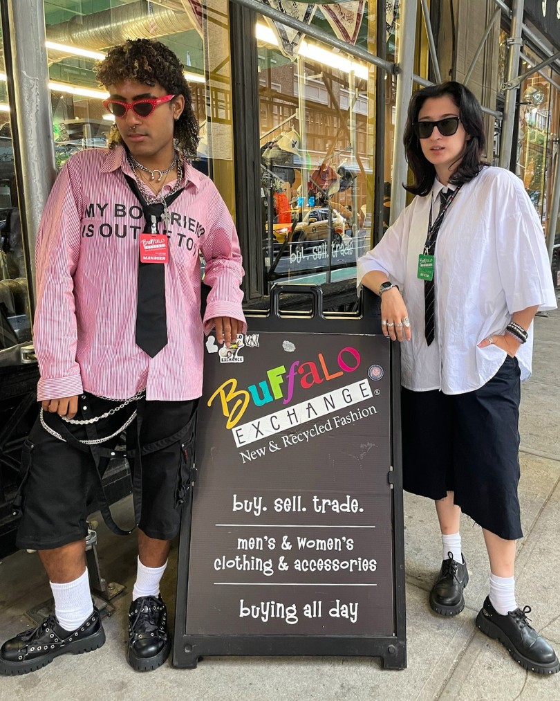 Two employees in front of Buffalo Exchange wearing wrinkled oversized button downs, loose ties, silver chains, black knee-length shorts and loafers with ankle socks Two employees in front of Buffalo Exchange wearing wrinkled oversized button downs, loose ties, silver chains, black knee-length shorts and loafers with ankle socks
