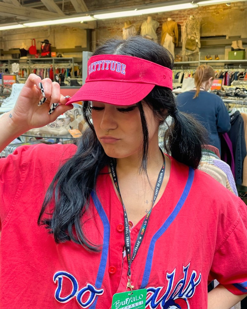 Employee at Buffalo Exchange in pigtails wearing a sporty red visor with "Hattitude" embroidered across the front and a matching Donald Duck baseball jersey Employee at Buffalo Exchange in pigtails wearing a sporty red visor with "Hattitude" embroidered across the front and a matching Donald Duck baseball jersey