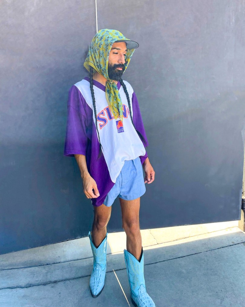 Person wearing an oversized Phoenix Suns tee shirt half tucked into blue shorts, turquoise western boots, and a baseball cap secured with a green floral scarf tied around their head Person wearing an oversized Phoenix Suns tee shirt half tucked into blue shorts, turquoise western boots, and a baseball cap secured with a green floral scarf tied around their head