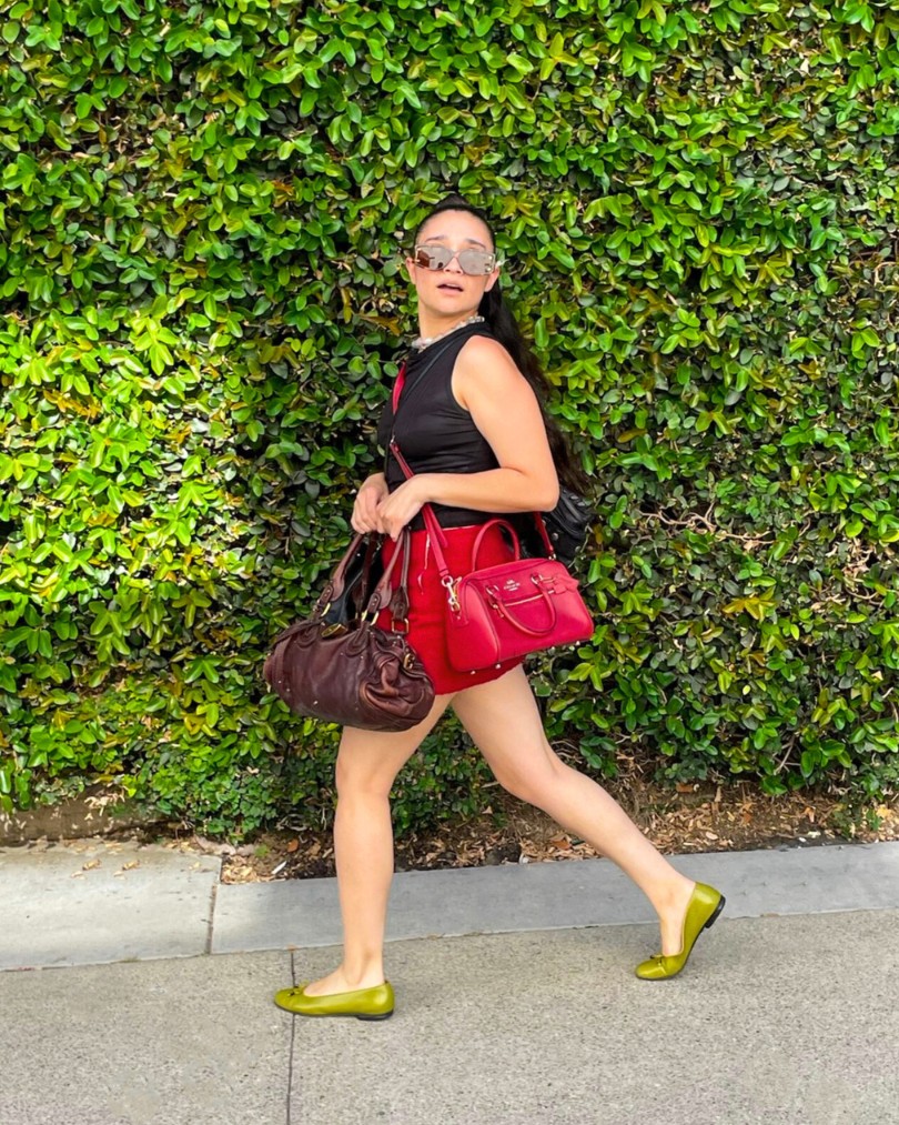 Person walking down a sidewalk wearing a black tank top, red mini skirt and olive ballet flats while carrying several designer purses from Chloe and Coach Person walking down a sidewalk wearing a black tank top, red mini skirt and olive ballet flats while carrying several designer purses from Chloe and Coach
