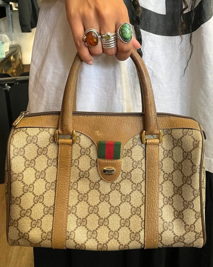 A close up of a hand adorned with chunky sterling silver stone rings carrying a vintage Gucci handbag in their iconic monogram print A close up of a hand adorned with chunky sterling silver stone rings carrying a vintage Gucci handbag in their iconic monogram print