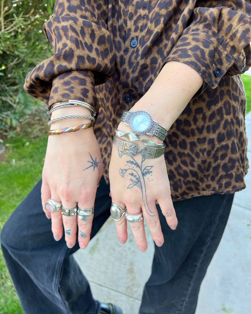 Close up of a person's hands with stick and poke tattoos & mixed metal jewelry including sterling silver bracelets, a vintage pearl-faced watch and chunky silver rings Close up of a person's hands with stick and poke tattoos & mixed metal jewelry including sterling silver bracelets, a vintage pearl-faced watch and chunky silver rings