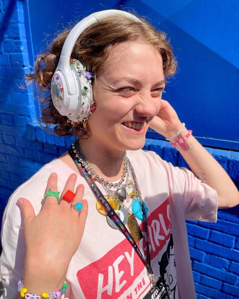 Person with maximalist style wearing a Betty Boop tee, over-the-ear headphones embellished with stickers, charm necklaces, beaded bracelets, and colorful rings Person with maximalist style wearing a Betty Boop tee, over-the-ear headphones embellished with stickers, charm necklaces, beaded bracelets, and colorful rings