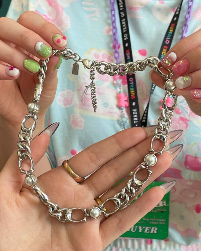 The hands of a Buffalo Exchange buyer with a cherry-inspired manicure holding up a Coach curb chain necklace with sterling silver links and pearl accents The hands of a Buffalo Exchange buyer with a cherry-inspired manicure holding up a Coach curb chain necklace with sterling silver links and pearl accents